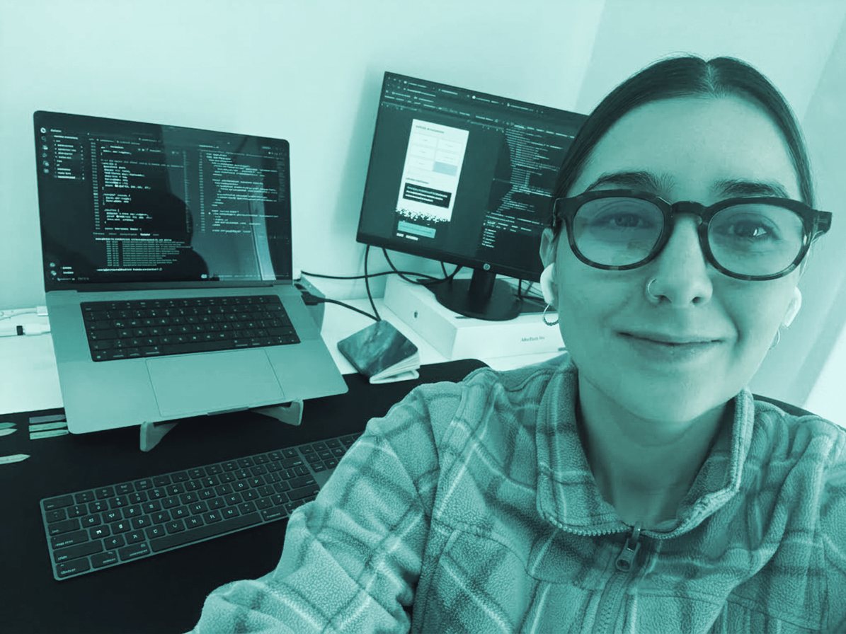 Retrato de quien desarrolla en Gradina, sonriendo frente a una laptop y un monitor con código.